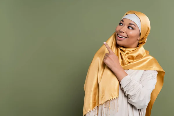 Позитивная многорасовая женщина в желтом хиджабе, указывающая пальцем на зеленый — стоковое фото