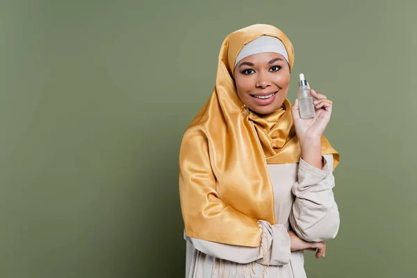 Positive multiracial woman in hijab holding serum on green background — Stock Photo