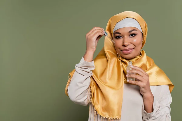 Junge multirassische Frau im Hijab mit Serum und Tropfer auf grünem Hintergrund — Stockfoto