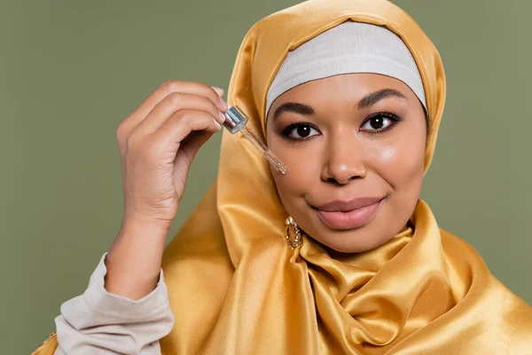Porträt einer multirassischen Frau im Hijab, die Tropfer mit Serum auf Grün isoliert hält — Stockfoto