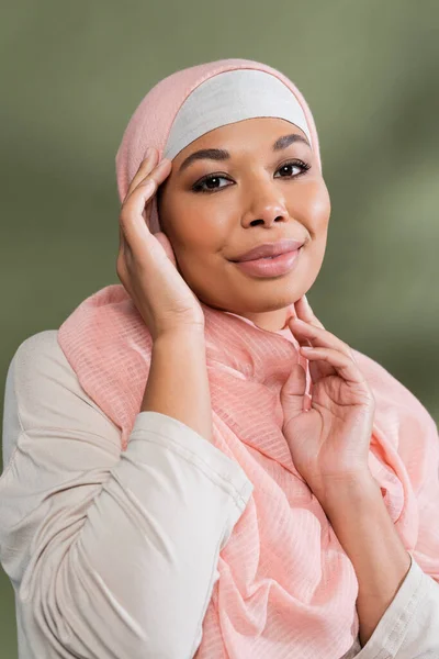 Femme musulmane multiraciale positive en hijab rose posant avec les mains près du visage sur fond vert — Photo de stock