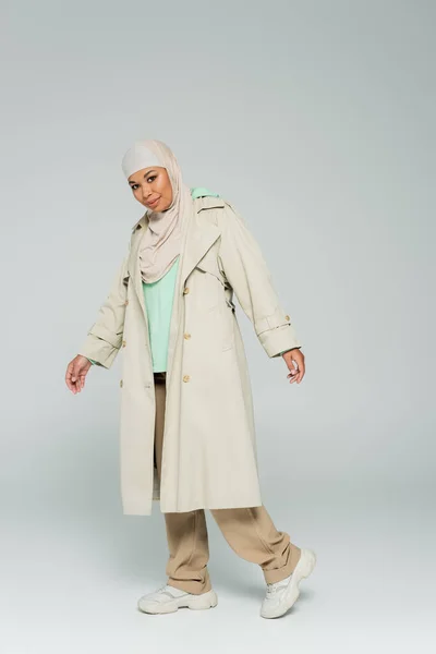Full length of multiracial muslim woman in trendy casual outfit and hijab looking at camera on grey background — Stock Photo