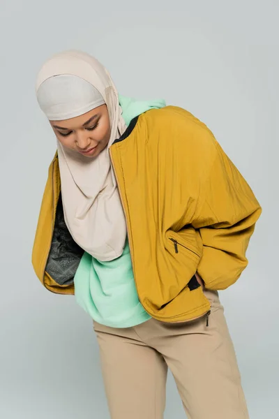 Trendige multirassische Frau in gelber Bomberjacke und Hijab posiert mit Hand in Tasche isoliert auf grau — Stockfoto
