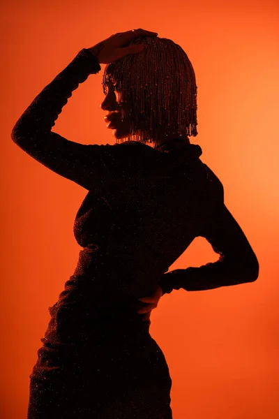 Shaded silhouette of sexy glamour woman in black dress and metallic headwear on orange background — Stock Photo