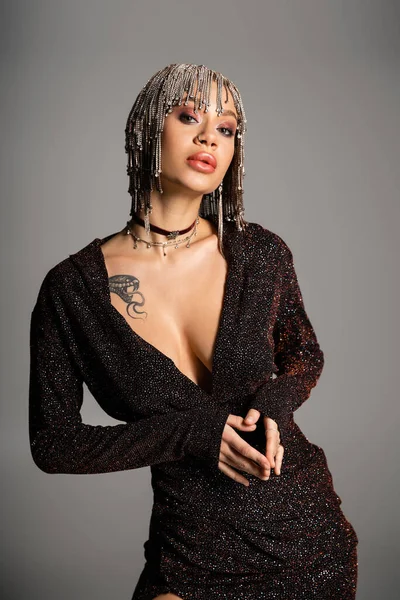 Tätowierte Frau mit sexy Körper posiert in schwarzem Lurexkleid und Schmuckperücke isoliert auf grau — Stockfoto