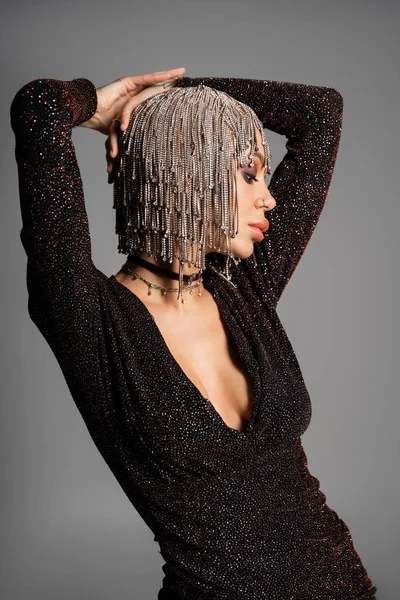 Femme de luxe en robe lurex noire et perruque métallique avec strass tenant les mains au-dessus de la tête isolé sur gris — Photo de stock