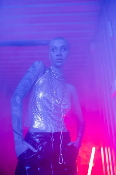 Sexy donna in top in metallo in piedi con le mani nelle tasche della gonna in pelle nera in illuminazione nebbiosa blu e rosa — Foto stock