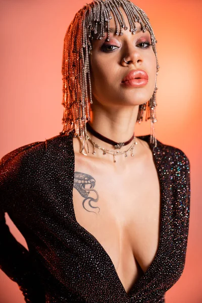 Портрет чувственной женщины с сексуальным татуированным телом, позирующим в черном платье и серебряном парике со стразами на коралловом розовом фоне — стоковое фото
