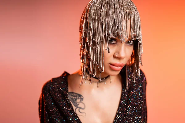 Portrait of sexy tattooed woman in metallic headwear with rhinestones looking at camera on coral pink background — Stock Photo