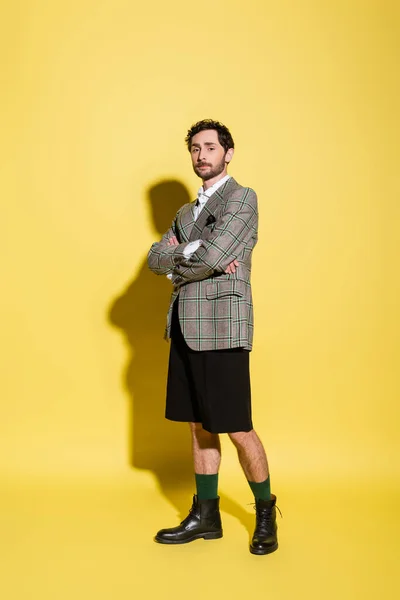 Full length of trendy model in jacket and shorts crossing arms on yellow background — Stock Photo