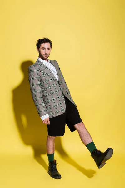 Longitud completa del modelo de moda en chaqueta y pantalones cortos de pie sobre fondo amarillo con sombra - foto de stock