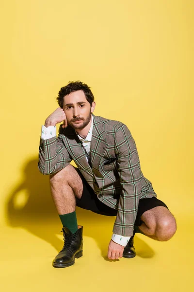 Stilvoller Mann in Stiefeln und Jacke posiert auf gelbem Hintergrund mit Schatten — Stockfoto
