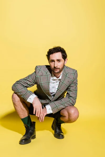 Hombre de moda en pantalones cortos y chaqueta posando sobre fondo amarillo con sombra - foto de stock