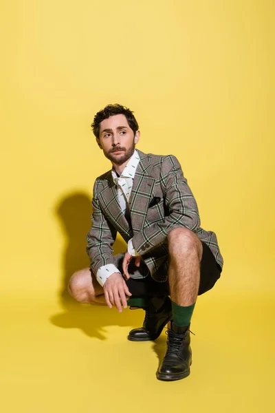 Uomo barbuto alla moda in giacca e pantaloncini in posa su sfondo giallo — Foto stock