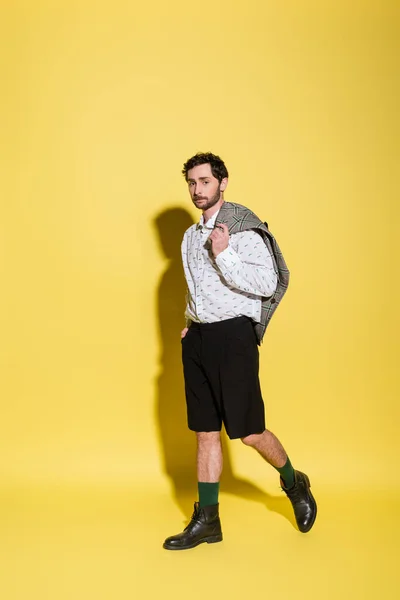 Повна довжина модного чоловіка тримає піджак під час ходьби на жовтому тлі — стокове фото