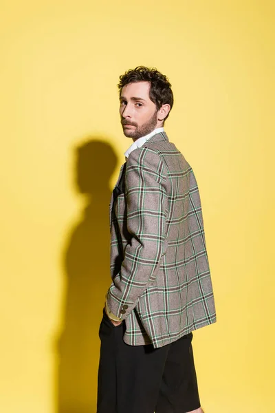 Homem na moda em jaqueta quadriculada olhando para a câmera no fundo amarelo — Fotografia de Stock