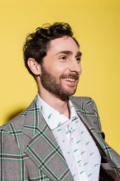 Retrato del hombre barbudo sonriente con camisa y chaqueta mirando hacia otro lado sobre fondo amarillo - foto de stock