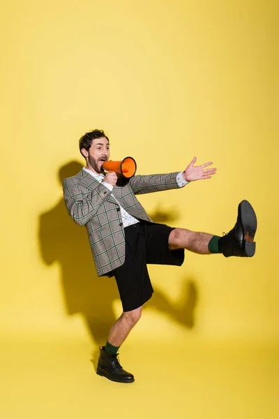 Excited and stylish man pointing with hand and talking at loudspeaker on yellow background — Stock Photo