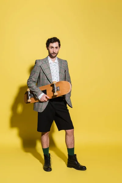 Full length of stylish model holding skateboard on yellow background — Stock Photo
