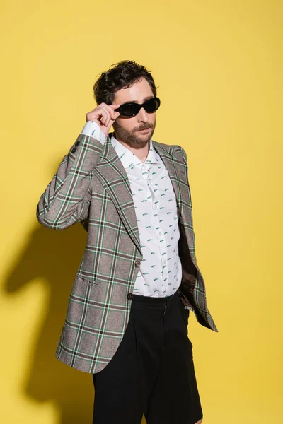Trendy charming guy in jacket holding sunglasses on yellow background — Stock Photo