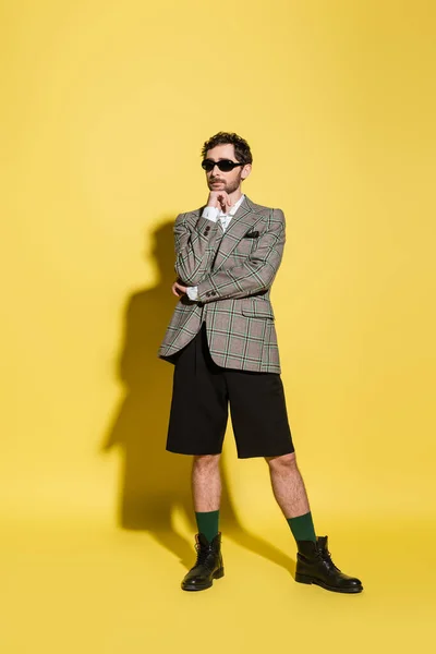 Charmanter Typ mit Sonnenbrille und Jacke posiert auf gelbem Hintergrund — Stockfoto