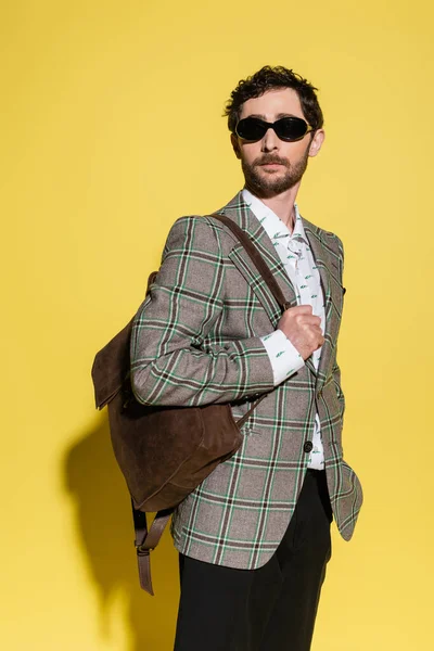 Модна модель в сонцезахисних окулярах позує з рюкзаком на жовтому тлі — стокове фото