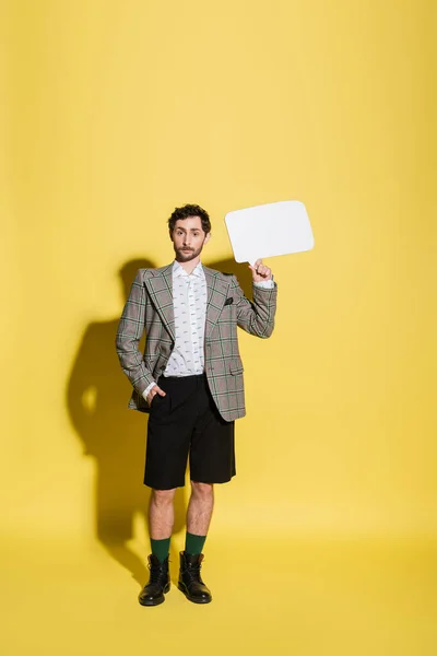 Trendmodel in Shorts und Jacke mit Sprechblase auf gelbem Hintergrund in voller Länge — Stockfoto