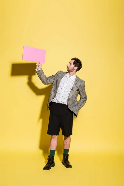 Side view of stylish model in blazer looking at speech bubble on yellow background — Stock Photo
