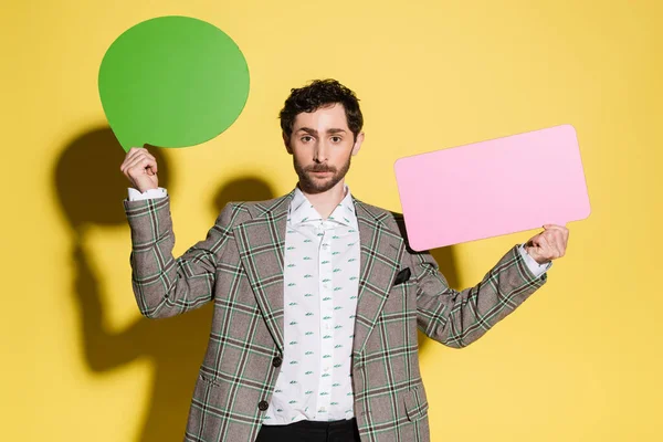Charming guy in jacket holding speech bubbles on yellow background — Stock Photo