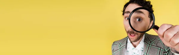 Vista de ângulo largo do homem na moda olhando através de lupa isolada em amarelo, banner — Stock Photo