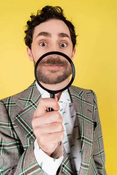 Wide angle view of stylish man in jacket holding magnifying glass isolated on yellow — Stock Photo