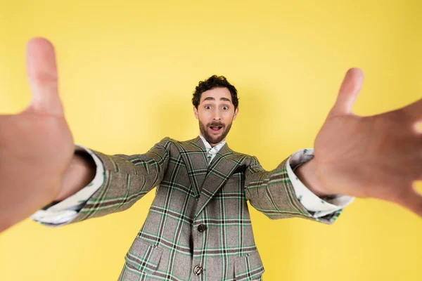 Visão de ângulo largo de homem elegante e animado em mãos de estender jaqueta na câmera isolada no amarelo — Fotografia de Stock