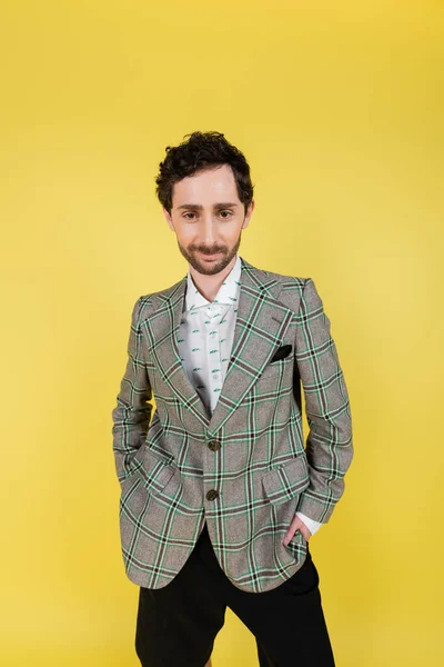 Elegante uomo in camicia e giacca a scacchi posa con le mani in tasche isolate sul giallo — Foto stock