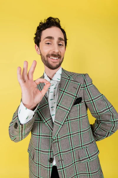 Wide angle view of smiling and stylish man showing ok gesture isolated on yellow — Stock Photo