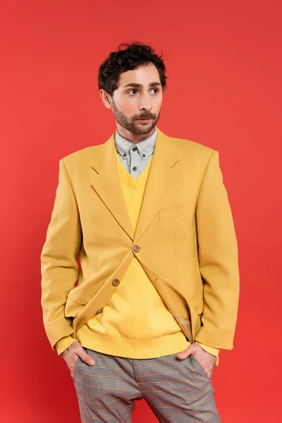 Charming chico en chaqueta amarilla cogido de la mano en bolsillos aislados en rojo - foto de stock