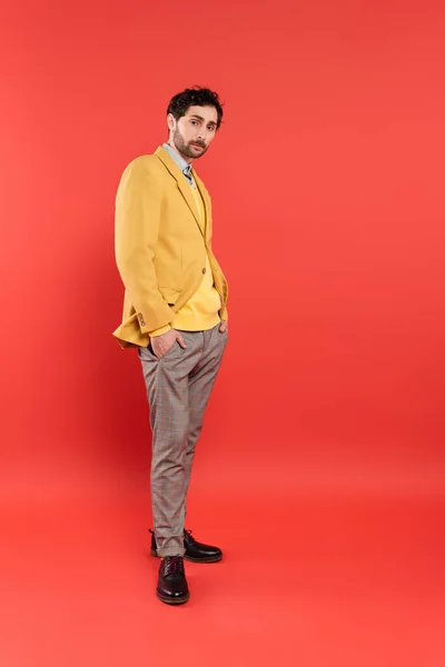 Full length of trendy model in jacket posing and looking at camera on coral red background — Stock Photo