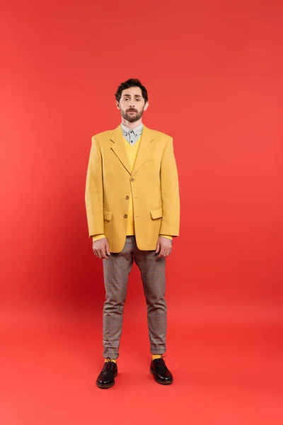 Longitud completa del modelo de moda en chaqueta amarilla de pie sobre fondo rojo - foto de stock