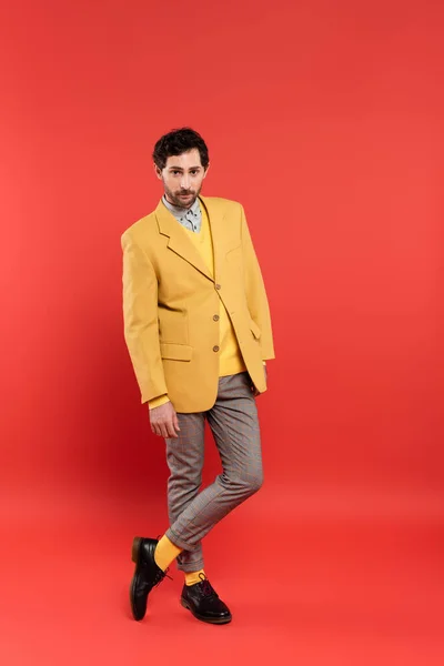Longitud completa del hombre de moda en pantalones a cuadros y chaqueta de pie sobre fondo rojo - foto de stock