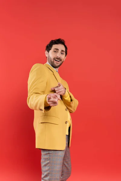 Homem alegre e na moda apontando para a câmera com os dedos isolados no vermelho — Fotografia de Stock