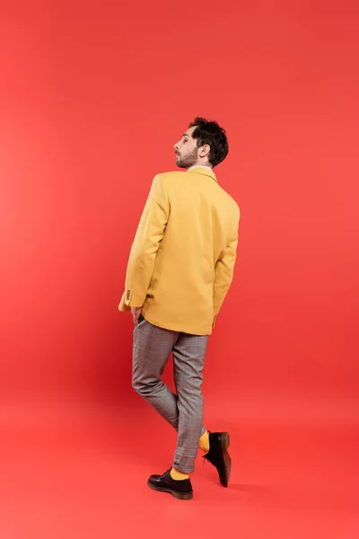 Vista lateral del hombre con estilo en chaqueta amarilla posando sobre fondo rojo coral - foto de stock