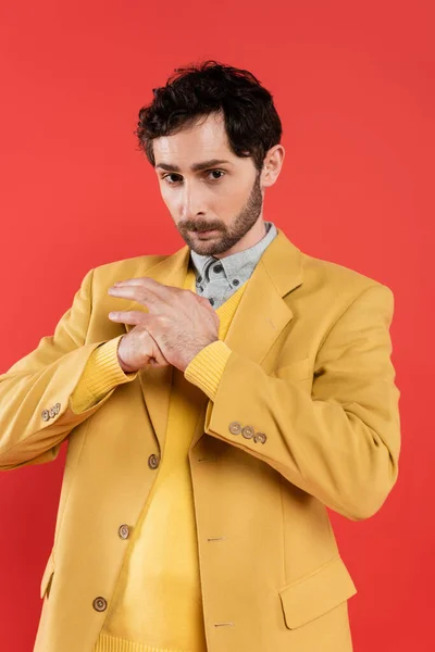 Retrato de tipo encantador en chaqueta amarilla apretando puño aislado en rojo - foto de stock
