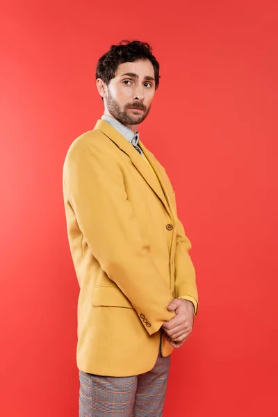 Elegante chico encantador en chaqueta amarilla de pie sobre fondo rojo coral - foto de stock