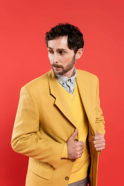 Ritratto di uomo barbuto alla moda che tocca giacca gialla isolata su corallo — Foto stock
