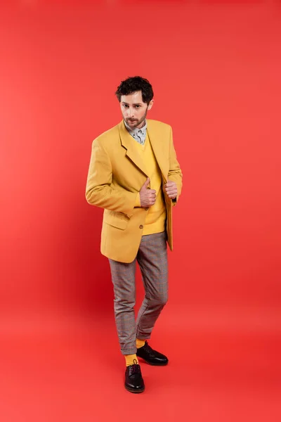 Full length of trendy model in vest and jacket posing on coral red background — Stock Photo