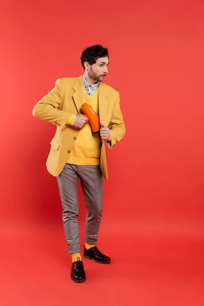 Modischer Mann versteckt Lautsprecher unter Jacke auf rotem Hintergrund — Stockfoto