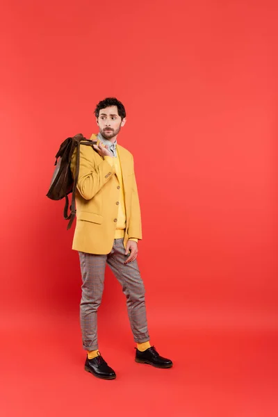 Full length of stylish model in yellow blazer holding backpack on coral red background — Stock Photo