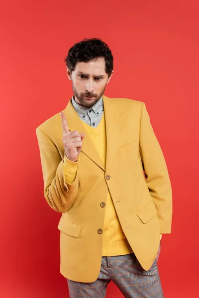 Hombre disgustado con chaqueta amarilla apuntando con el dedo mientras advierte aislado en rojo coral - foto de stock