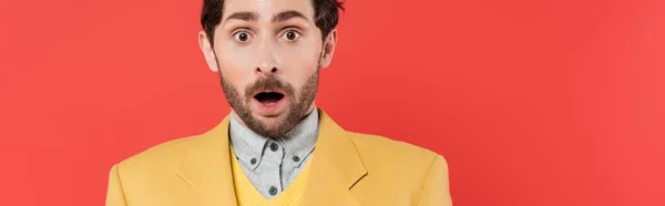 Shocked man in yellow blazer standing with opened mouth and looking at camera on coral background, banner — Stock Photo