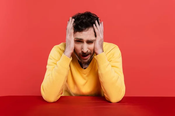 Bearded man in yellow long sleeve jumper touching head while having hangover isolated on red coral background — Stock Photo