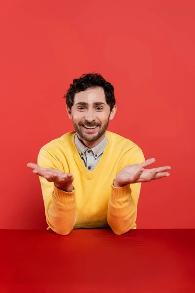 Uomo spensierato in giallo maglione a maniche lunghe gesticolando su sfondo corallo rosso — Foto stock